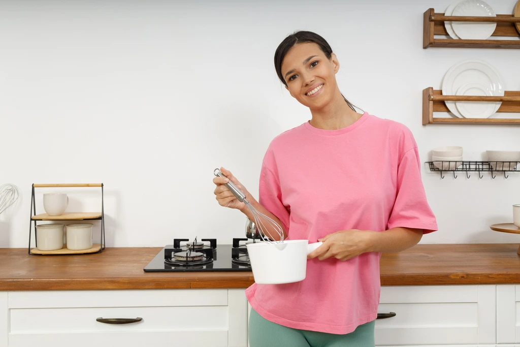 Aria Thompson, founder of Cooking Zenith, smiling warmly in her kitchen while holding a whisk and a small white saucepan.