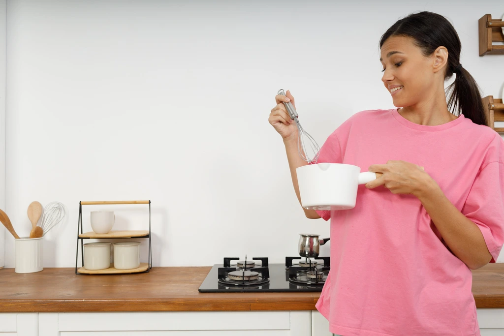 Aria Thompson of Cooking Zenith smiling as she looks down into a saucepan, happily whisking the contents over the stove.