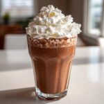 A tall glass filled with thick, blended frozen hot chocolate topped generously with whipped cream.