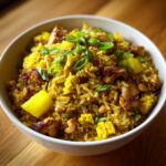 A close-up of vibrant yellow pineapple fried rice served in a white bowl, topped with green onions.