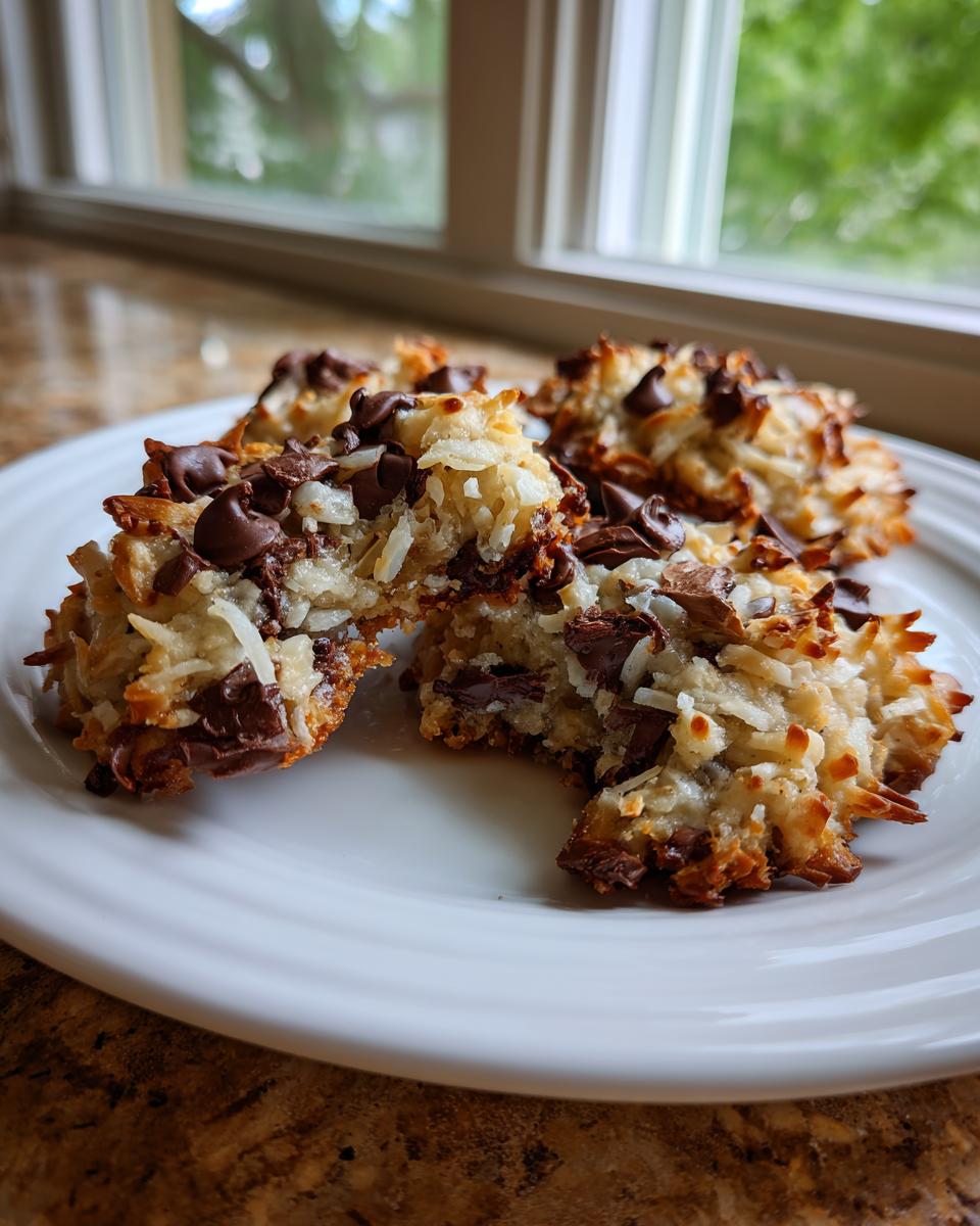 Four baked almond joy cookies made with shredded coconut and chocolate chips, resting on a white plate.