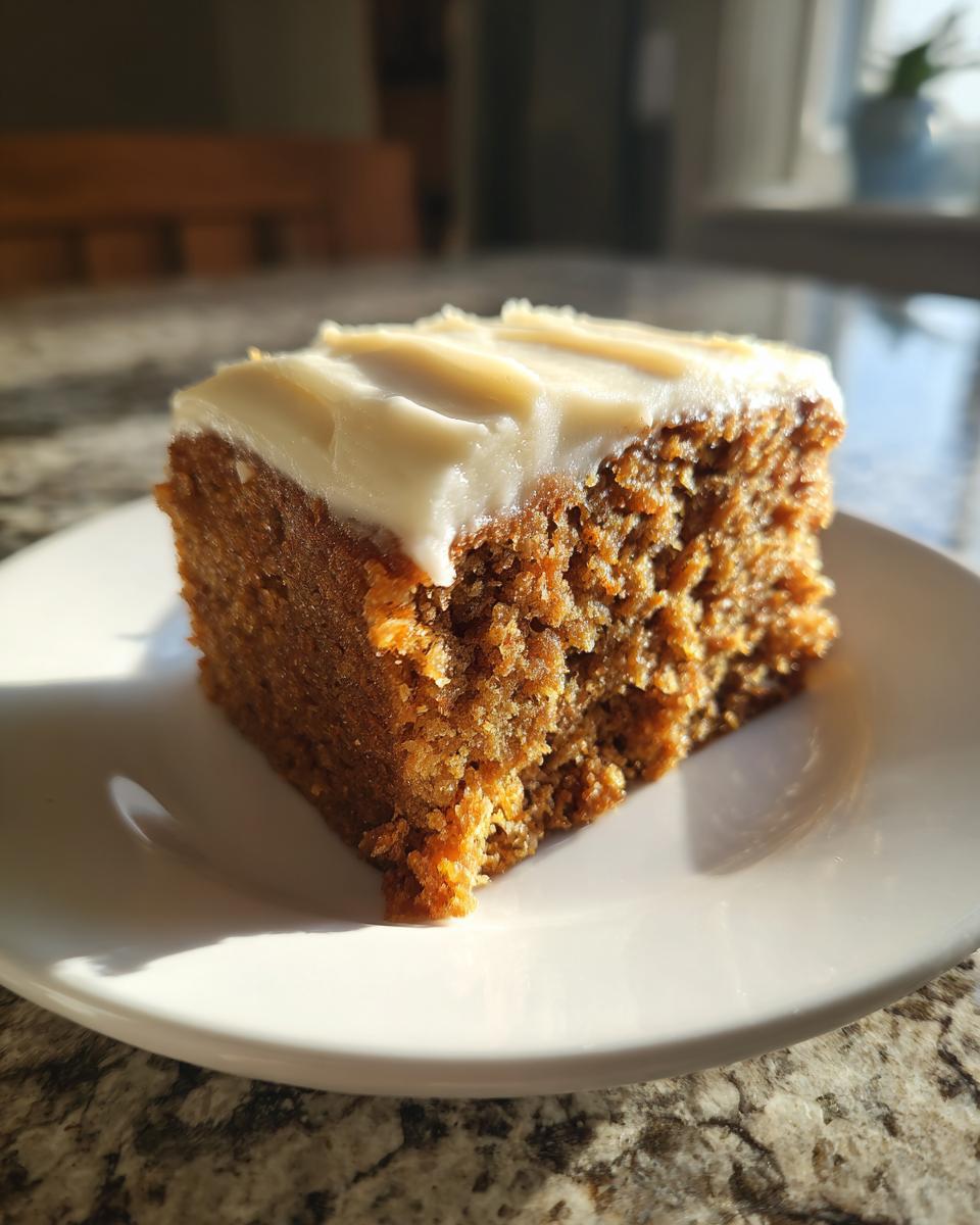 Close-up of a moist slice of amazing 1 spice cake topped with thick white cream cheese frosting, sitting on a white plate.