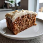 A close-up of a moist slice of amazing 1 spice cake topped with thick, creamy frosting on a white plate.