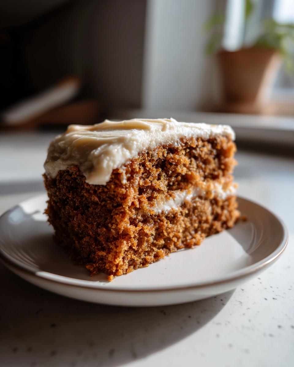 A close-up, sunlit slice of moist spice cake layered with cream cheese frosting on a small white plate.