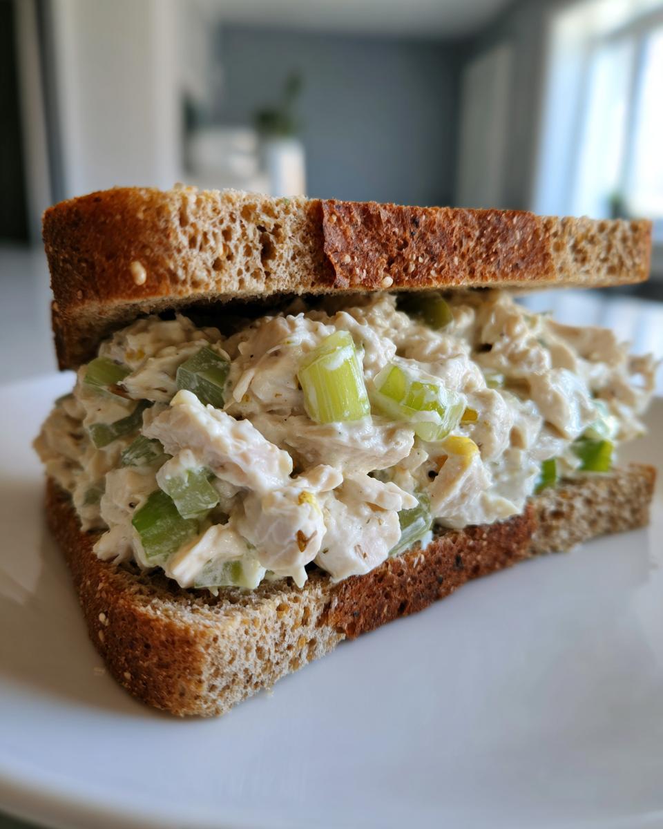 A close-up of an amazing chicken salad sandwich made with creamy filling and crunchy celery on dark whole wheat bread.