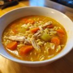 Close-up of a white bowl filled with rich broth, shredded chicken, carrots, celery, and egg noodles in this amazing chicken soup.