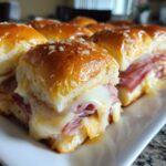 Close-up of gooey melted cheese and ham inside freshly baked grinder sliders on a white platter.