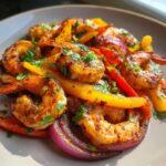 Close-up of perfectly cooked, seasoned shrimp fajitas with colorful bell peppers and red onion, garnished with cilantro.