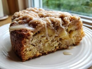 Close-up of a moist slice of apple crumb cake topped with streusel and a vanilla icing drizzle.