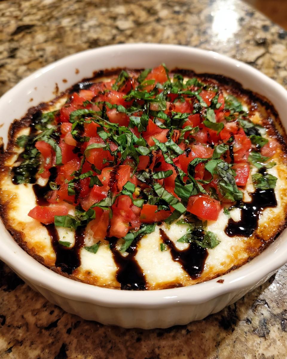 Close-up of hot, baked 3-cheese bruschetta dip topped with diced tomatoes, basil, and balsamic glaze.
