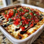 Close-up of a hot, baked 3-cheese bruschetta dip topped with fresh diced tomatoes, basil, and balsamic glaze.