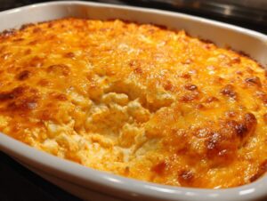 Close-up of a baked Buffalo chicken dip with a bubbly, golden-brown melted cheese topping in a white casserole dish.