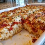 A close-up view of a freshly baked chicken Parmesan casserole showing shredded chicken filling, marinara sauce, and a golden, cheesy, breadcrumb topping.