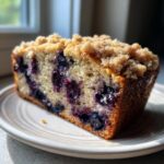A close-up slice of moist blueberry banana bread topped with a crunchy streusel topping, resting on a plate.