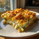 A close-up, sunlit slice of creamy broccoli cheese casserole topped with golden, crunchy cornflakes.