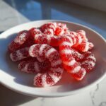 A pile of bright red and white striped, sugar-coated Candy Cane Fireball Gummies resting on a white plate.