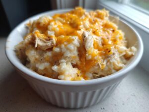 Close-up of a white ramekin filled with creamy chicken and rice casserole topped with melted cheddar cheese.