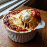 Close-up of a hot, bubbly pizza dip with extreme cheese pull in a white ramekin.