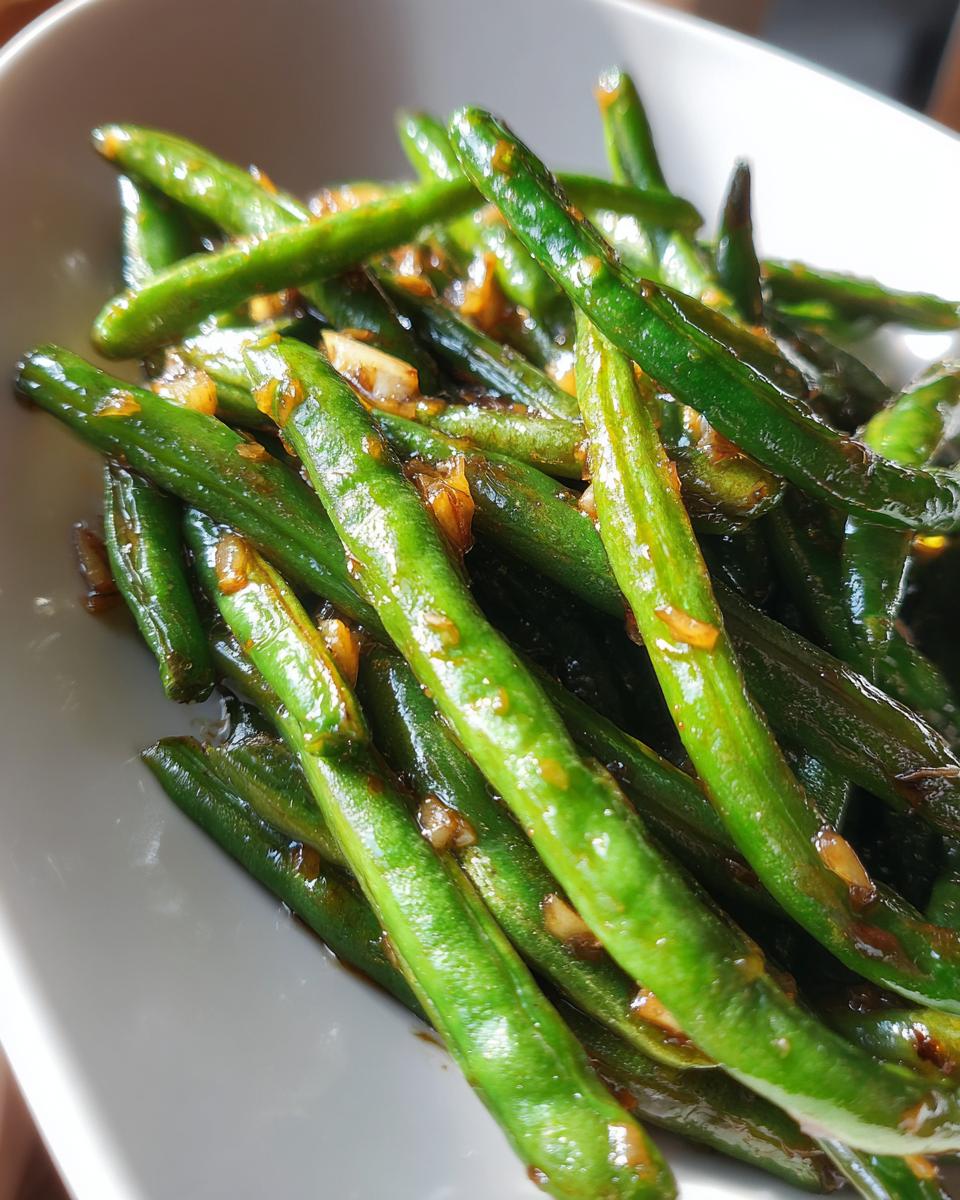 Vibrant, glossy green beans coated in a savory brown garlic sauce, ready to serve.