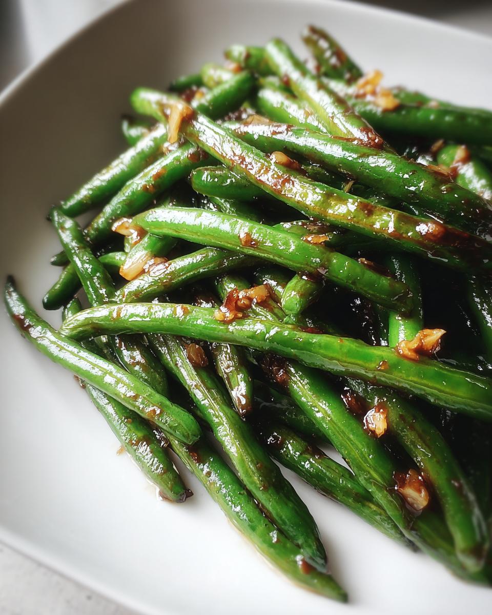 Close-up of vibrant, glossy chinese green beans with garlic sauce served on a white plate.