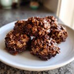 A close-up of several rich, chocolatey no bake cookies made with oats, piled on a white plate.