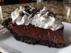 A decadent slice of Christmas chocolate cream pie featuring a dark chocolate filling, cookie crust, and whipped cream topping.