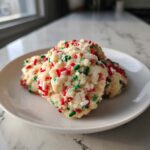 Three soft, pale christmas sprinkle sugar cookies loaded with red, green, and white sprinkles on a white plate.