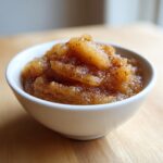 A close-up of chunky, homemade applesauce heavily spiced with cinnamon, served in a small white bowl.