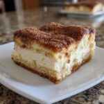 A close-up of a square slice of churro cheesecake with a thick cream cheese layer and cinnamon-sugar topping.