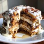 Cross-section view of a tall stack of cinnamon roll pancakes layered with cream cheese frosting and drizzled with icing.
