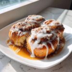 Four gooey cinnamon rolls with white icing and caramel sauce, perfect for cinnamon rolls with heavy cream recipes.