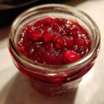 Close-up view of vibrant, chunky homemade christmas jam filled in a small glass jar.
