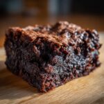 A close-up, mouthwatering shot of a rich, dark chocolate Cottage Cheese Microwave Brownie square on a wooden surface.