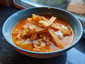 Close-up of creamy chicken tortilla soup topped with crispy tortilla strips and sour cream.