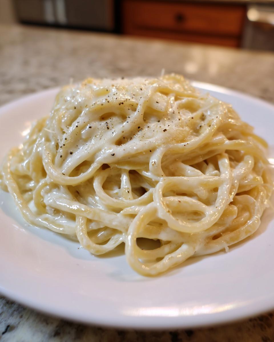 Close-up of spaghetti coated generously in rich, creamy homemade alfredo sauce, topped with black pepper.