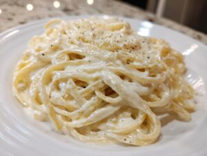 Close-up of fettuccine pasta generously coated in creamy homemade alfredo sauce, topped with black pepper.