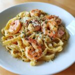 A close-up of creamy shrimp alfredo pasta topped with grated Parmesan cheese and parsley.