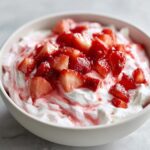 A close-up of creamy white strawberry cheesecake dip topped with macerated, chopped fresh strawberries.