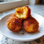 Close-up of crispy fried rice balls, one broken open revealing melted cheese inside.