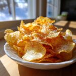 A close-up of a white bowl filled with golden, crunchy air fryer potato chips seasoned with salt.
