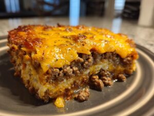 Close-up of a hearty slice of Dorito Casserole featuring layers of seasoned ground beef and a thick, melted cheddar cheese topping.
