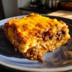 A generous slice of Dorito Casserole featuring layers of rice, seasoned ground beef, and melted cheddar cheese on a blue plate.