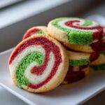 A stack of colorful pinwheel cookies featuring red, green, and white swirls, resting on a white plate.
