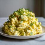 A large mound of creamy, yellow egg salad mixed with chopped celery and topped generously with fresh dill.
