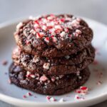 A stack of three fudgy chocolate peppermint cookies topped with crushed candy canes.