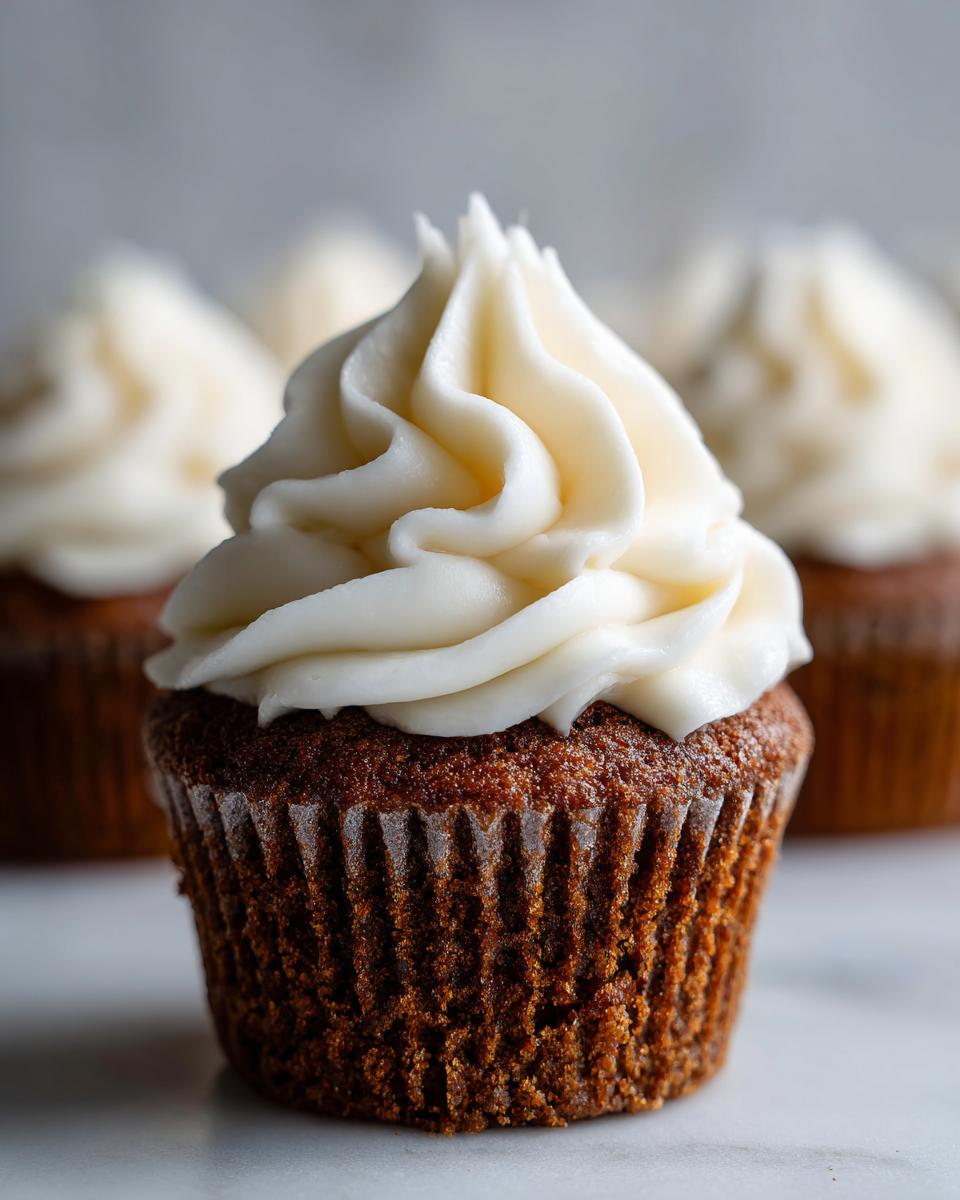 A close-up of a rich, dark gingerbread cupcakes topped with a swirl of creamy white frosting.