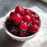 Close-up of glossy, bright red homemade cherry pie filling served in a small white bowl.