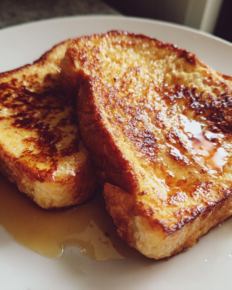 Close-up of two slices of perfectly cooked, golden brown french toast drizzled with maple syrup.