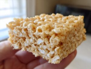 Close-up of a thick, gooey peanut butter rice krispie treats square being held in a hand.