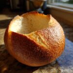 A freshly baked, round bread bowl with the top cut out, ready to be filled with soup.
